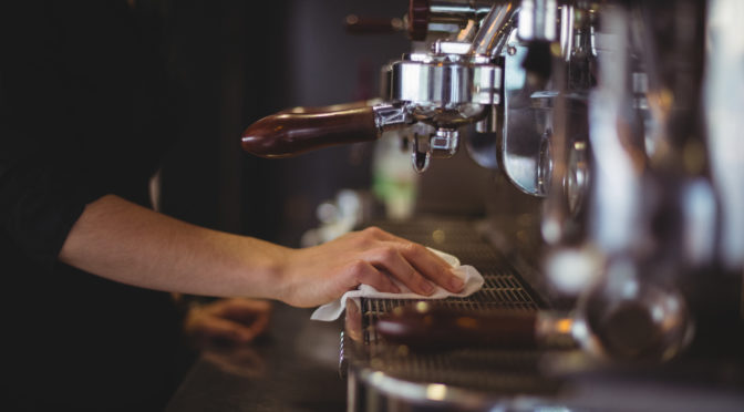 Mid section of waitress wiping espresso machine with napkin in cafÃ©